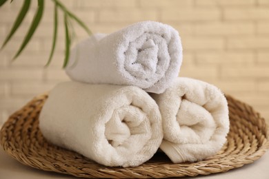 Rolled terry towels and green leaves on white table near brick wall indoors, closeup