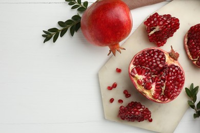Photo of Fresh pomegranates and branches on white wooden table, flat lay. Space for text
