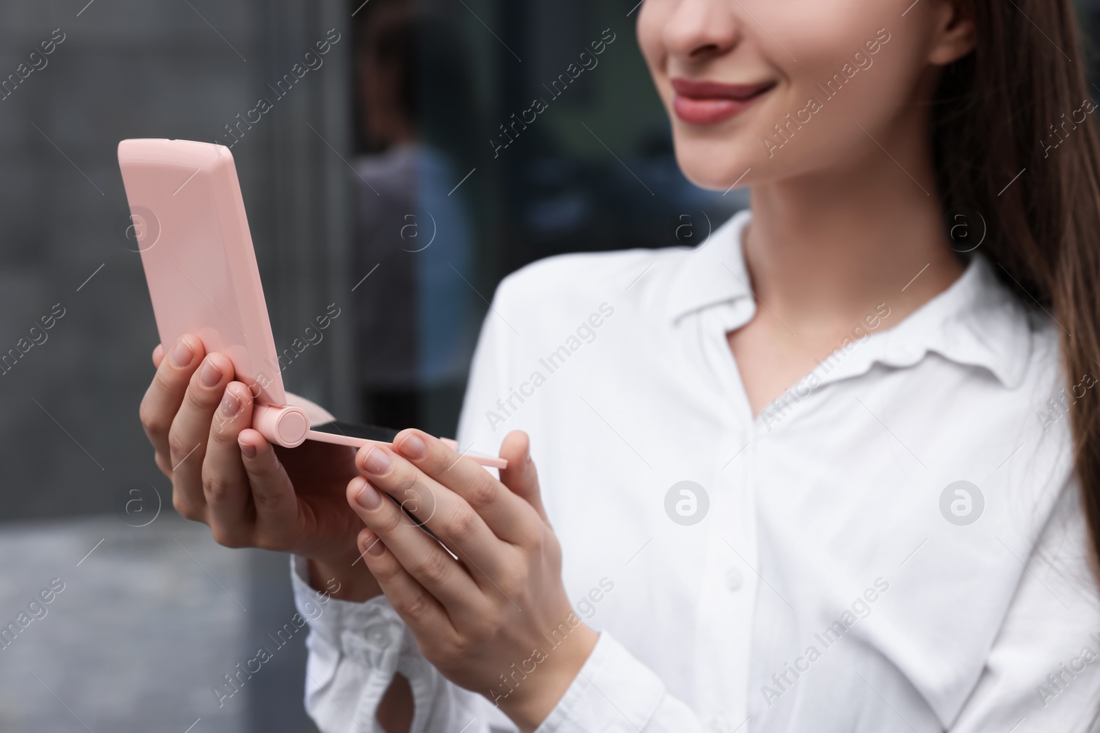 Photo of Young woman looking at herself in cosmetic pocket mirror outdoors, closeup