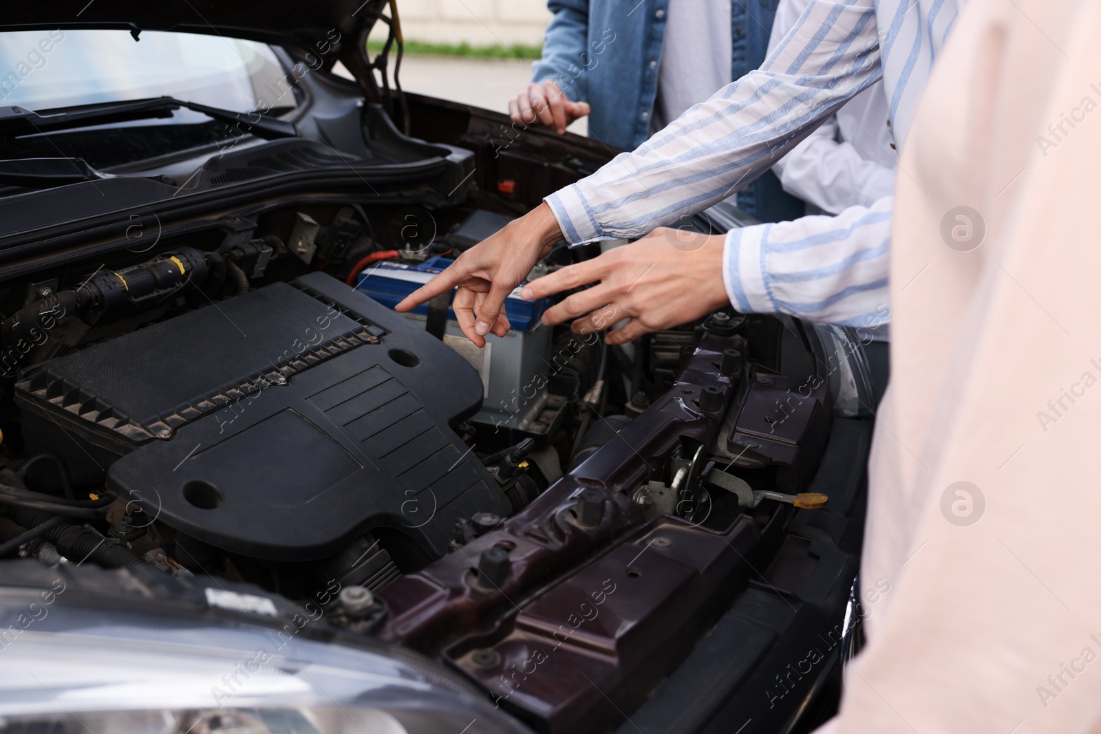 Photo of Driving school. Teacher explaining car engine to group outdoors, closeup