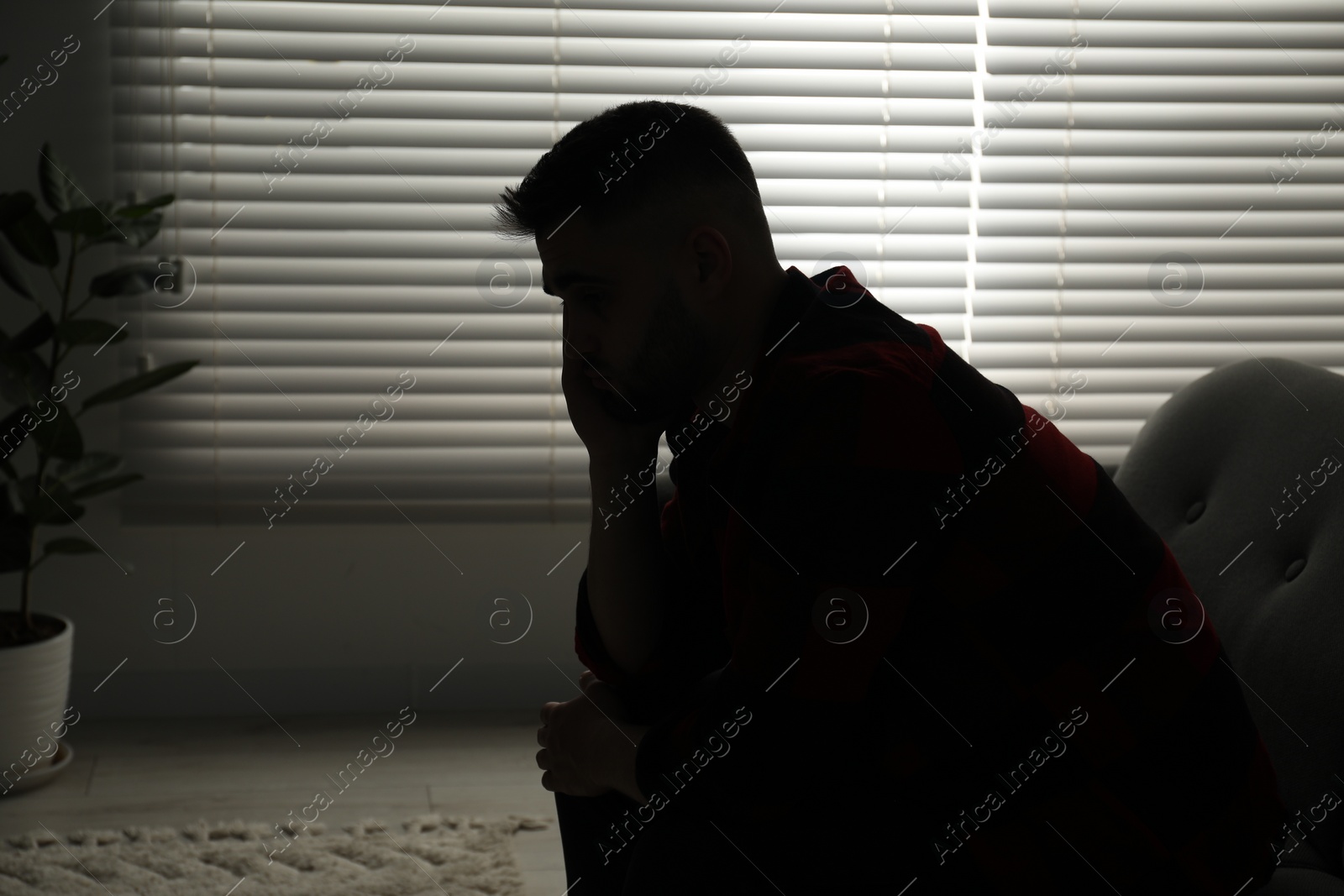 Photo of Silhouette of sad man near closed blinds indoors. Space for text