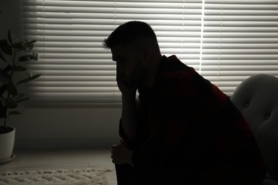 Photo of Silhouette of sad man near closed blinds indoors. Space for text