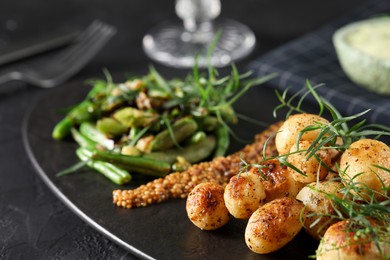 Delicious grilled potatoes with tarragon served on black textured table, closeup