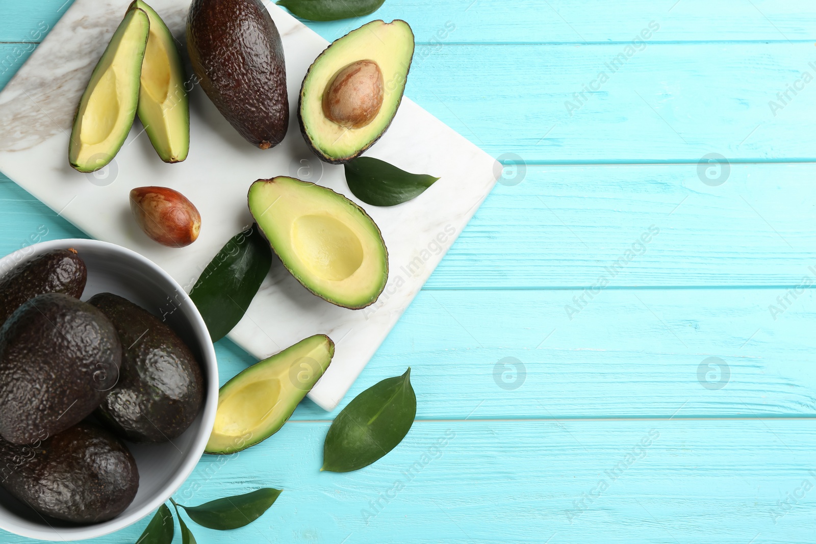 Photo of Whole and cut avocados on turquoise wooden table, flat lay. Space for text