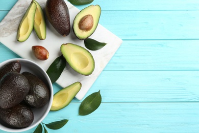 Whole and cut avocados on turquoise wooden table, flat lay. Space for text