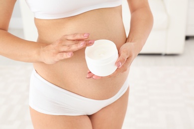 Photo of Pregnant woman holding body cream at home, closeup