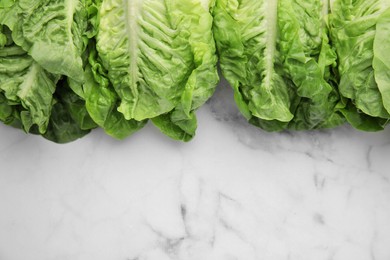 Photo of Fresh green romaine lettuces on white marble table, flat lay. Space for text