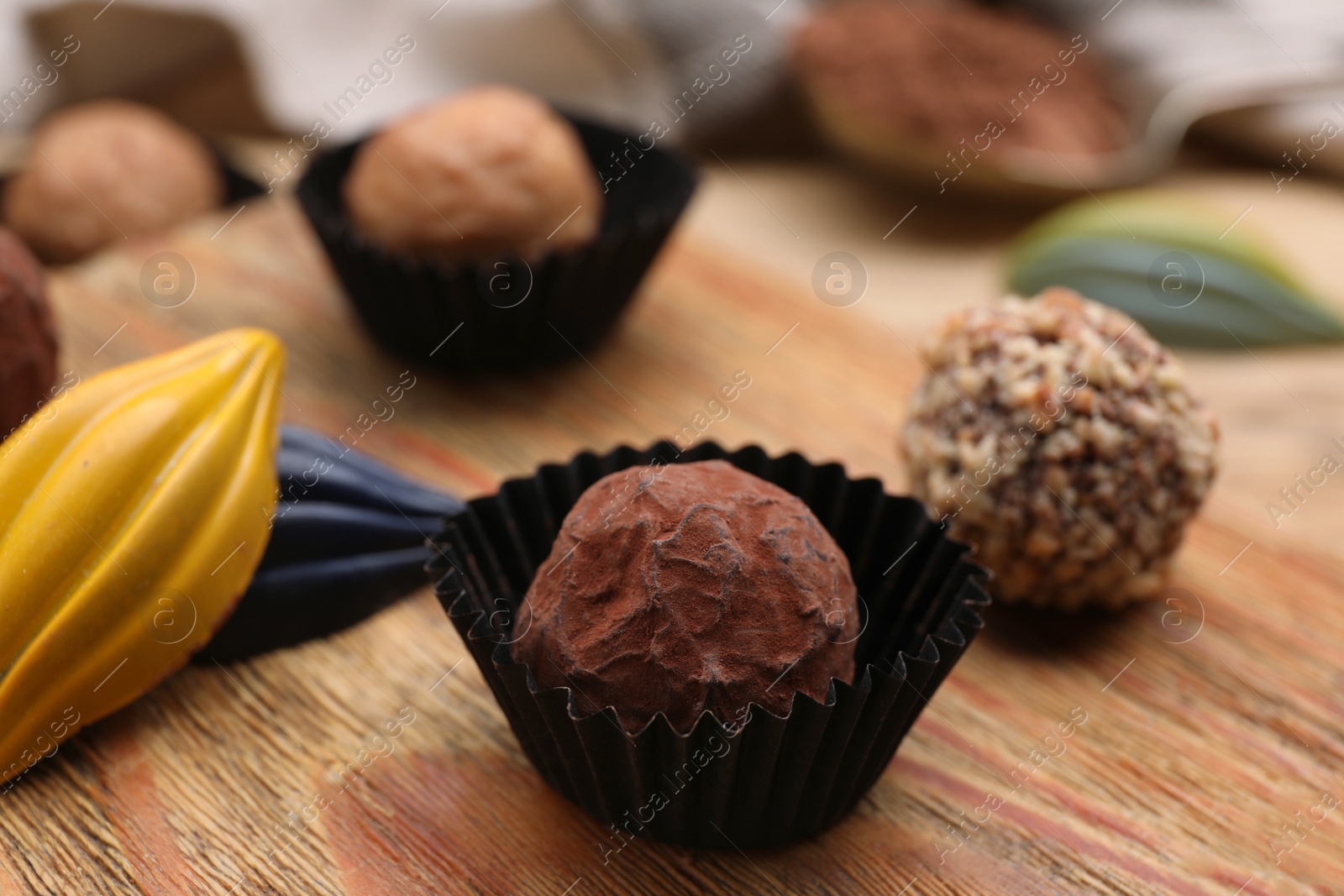Photo of Different tasty chocolate candies on wooden board, closeup