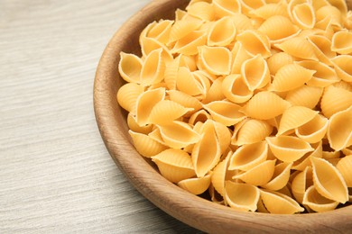 Photo of Raw conchiglie pasta in bowl on light grey wooden table, closeup