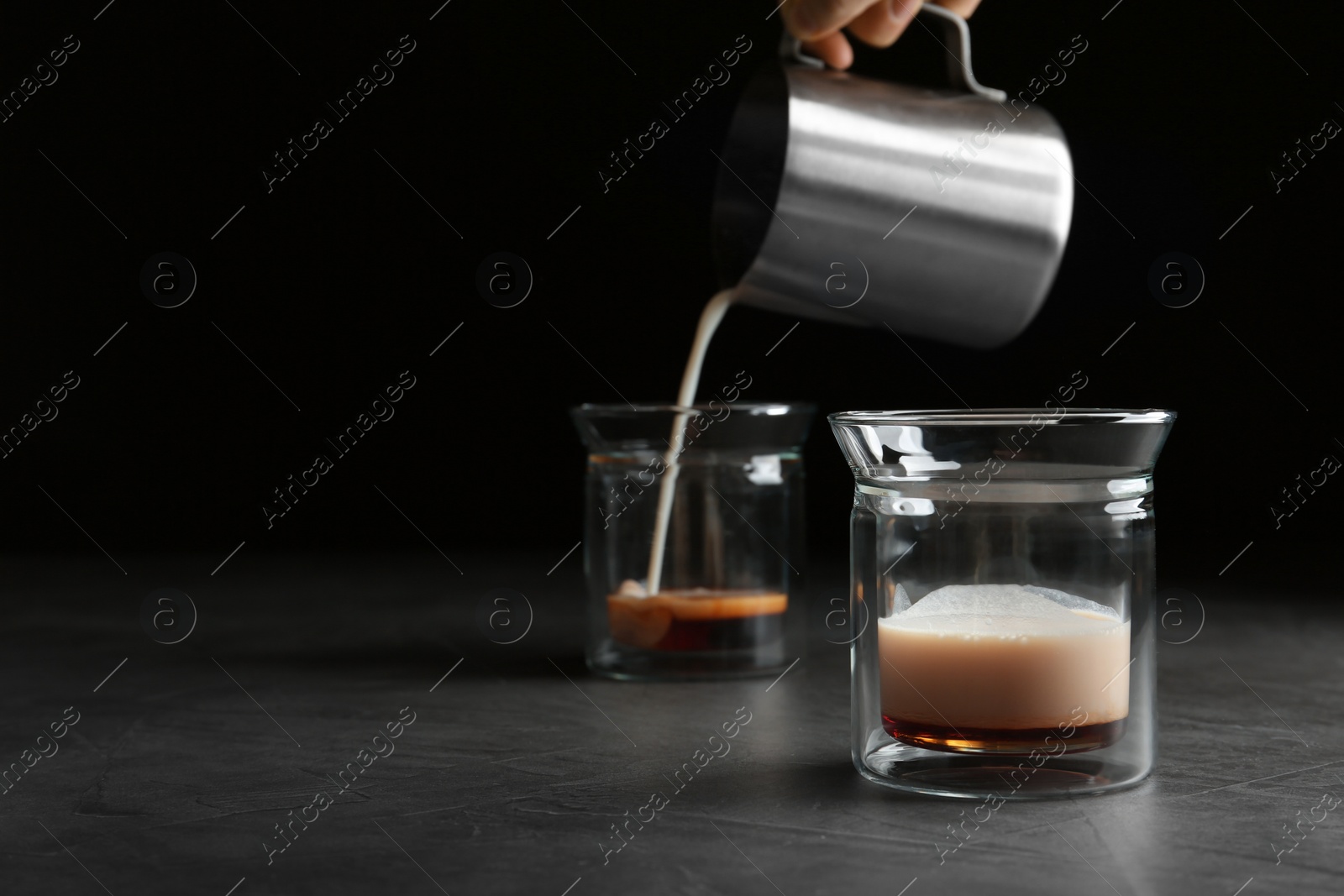 Photo of Pouring milk into glass on grey table, space for text. Preparing aromatic coffee