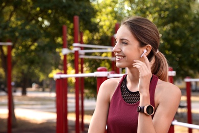 Photo of Young woman with wireless headphones listening to music on sports ground. Space for text