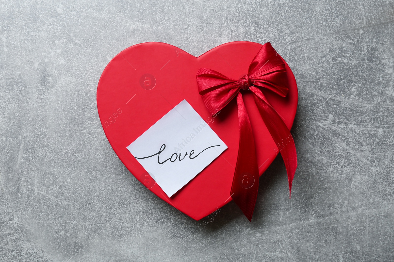 Photo of Heart shaped gift box and sticker with handwritten word LOVE on grey background, top view