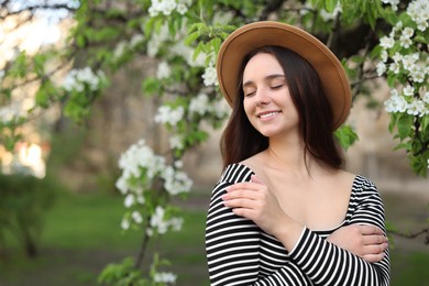Photo of Beautiful woman in hat near blossoming tree on spring day, space for text