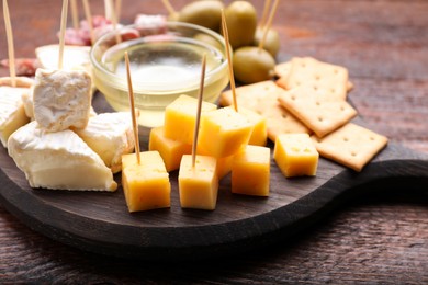 Photo of Toothpick appetizers. Pieces of different cheese on wooden table, closeup