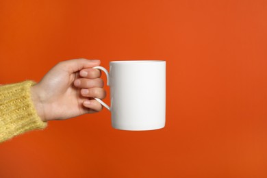 Photo of Woman holding white mug on orange background, closeup. Space for text