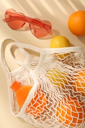 String bag with fresh fruits, sunscreen and sunglasses on beige background, flat lay