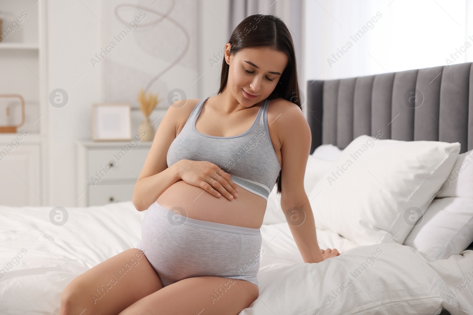 Photo of Beautiful pregnant woman in comfortable maternity underwear on bed at home