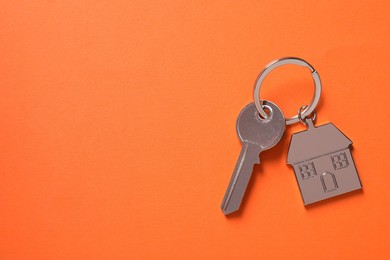 Photo of Metallic key with keychain in shape of house on orange background, top view. Space for text