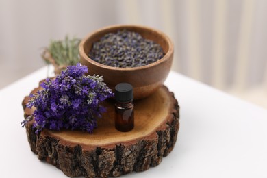 Bottle of aromatic essential oil, stump and beautiful flowers on white table