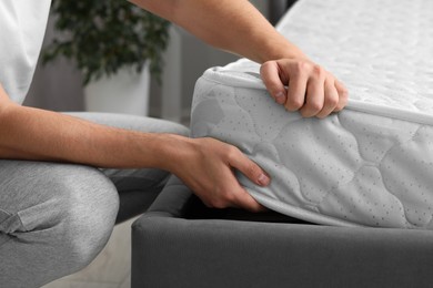 Photo of Man putting soft mattress on bed, closeup