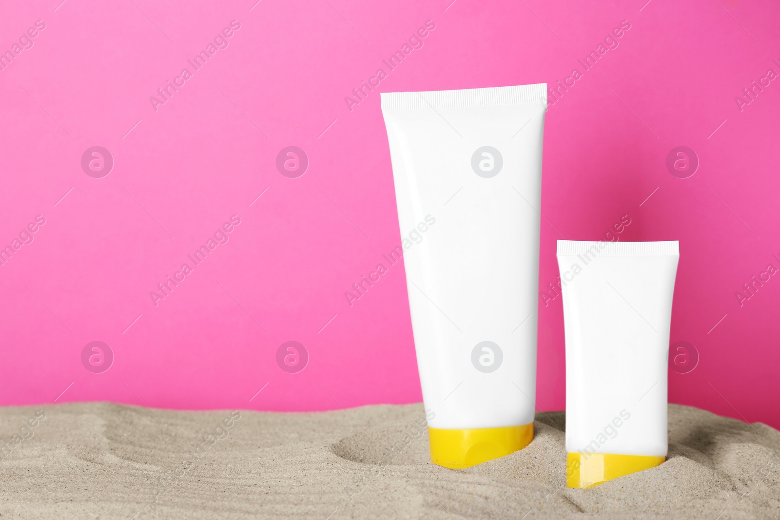 Photo of Different suntan products on sand against pink background. Space for text