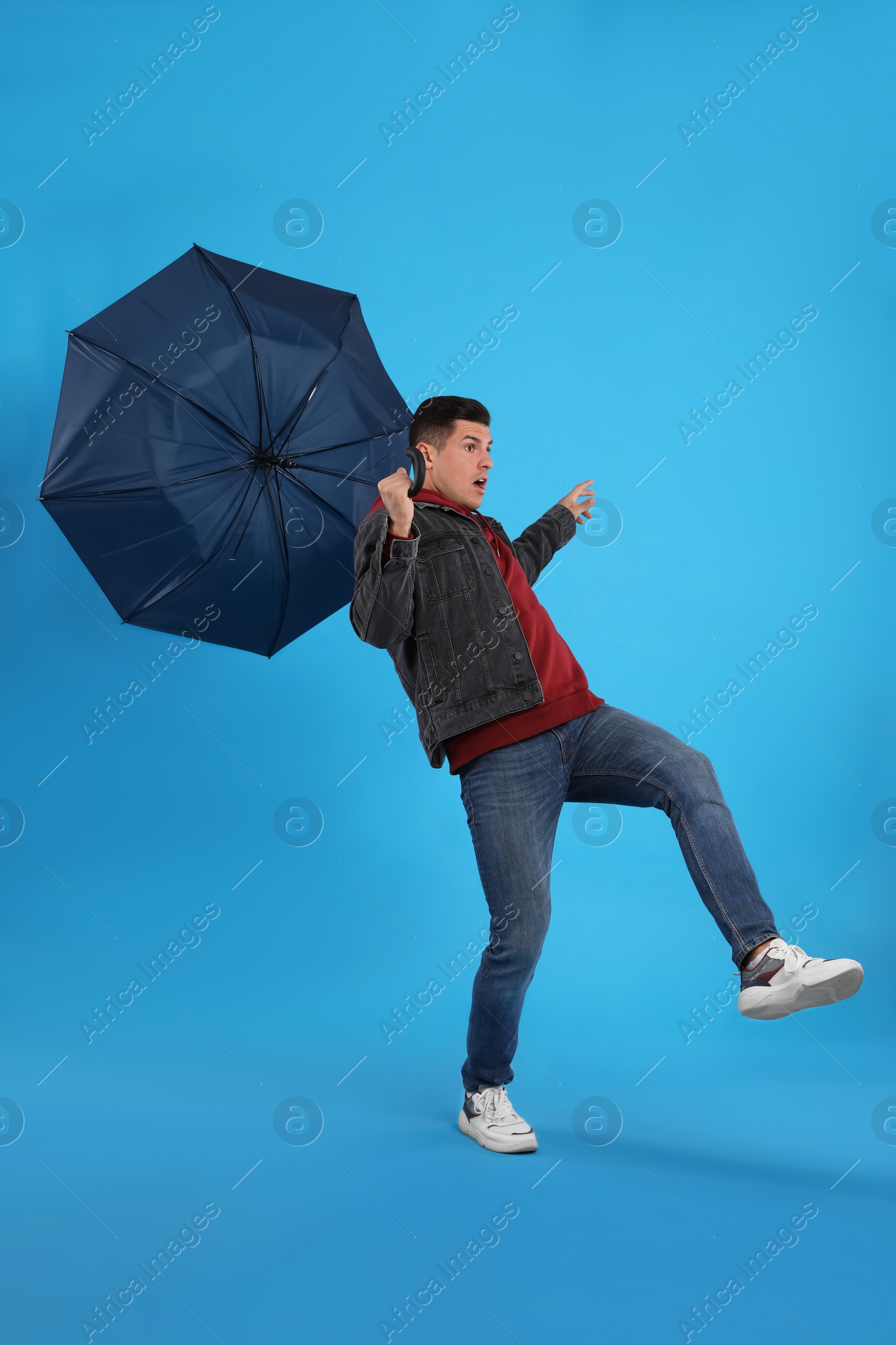 Photo of Man with umbrella caught in gust of wind on light blue background