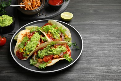 Photo of Delicious tacos with guacamole, meat and vegetables on wooden table, space for text