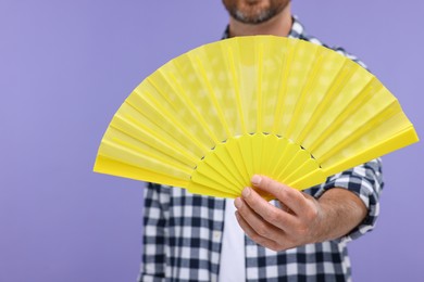 Photo of Man holding hand fan on purple background, closeup