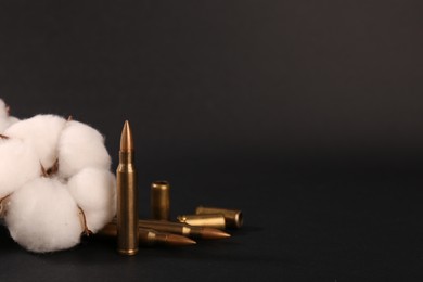 Photo of Bullets, cartridge cases and beautiful cotton flower on black background. Space for text