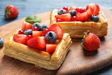 Photo of Fresh delicious puff pastry with sweet berries on wooden board, closeup