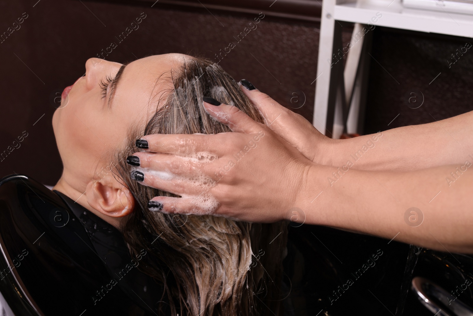 Photo of Professional hairdresser washing woman's hair at sink in salon