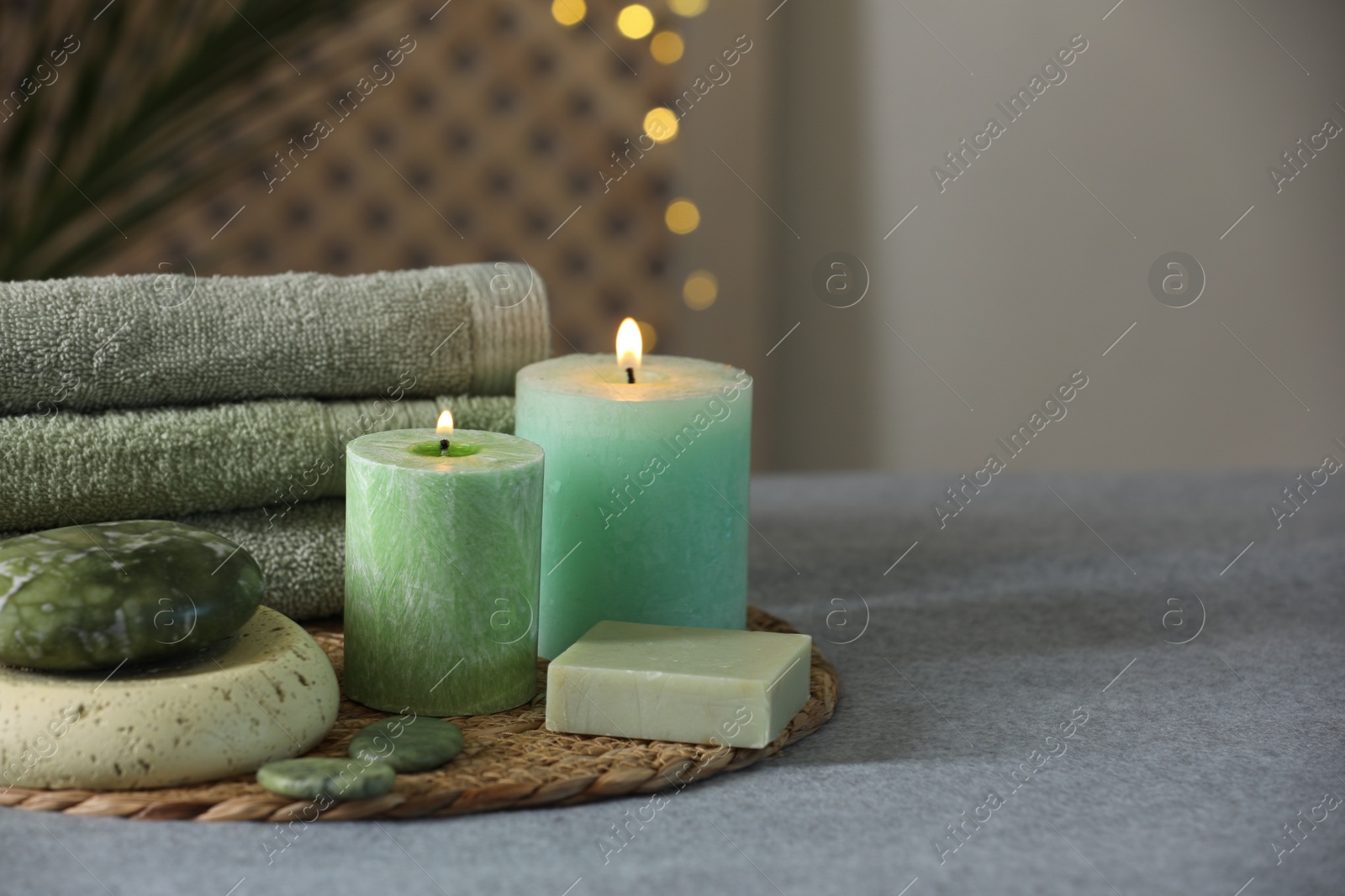Photo of Spa composition. Burning candles, stones, soap and towels on soft grey surface, space for text