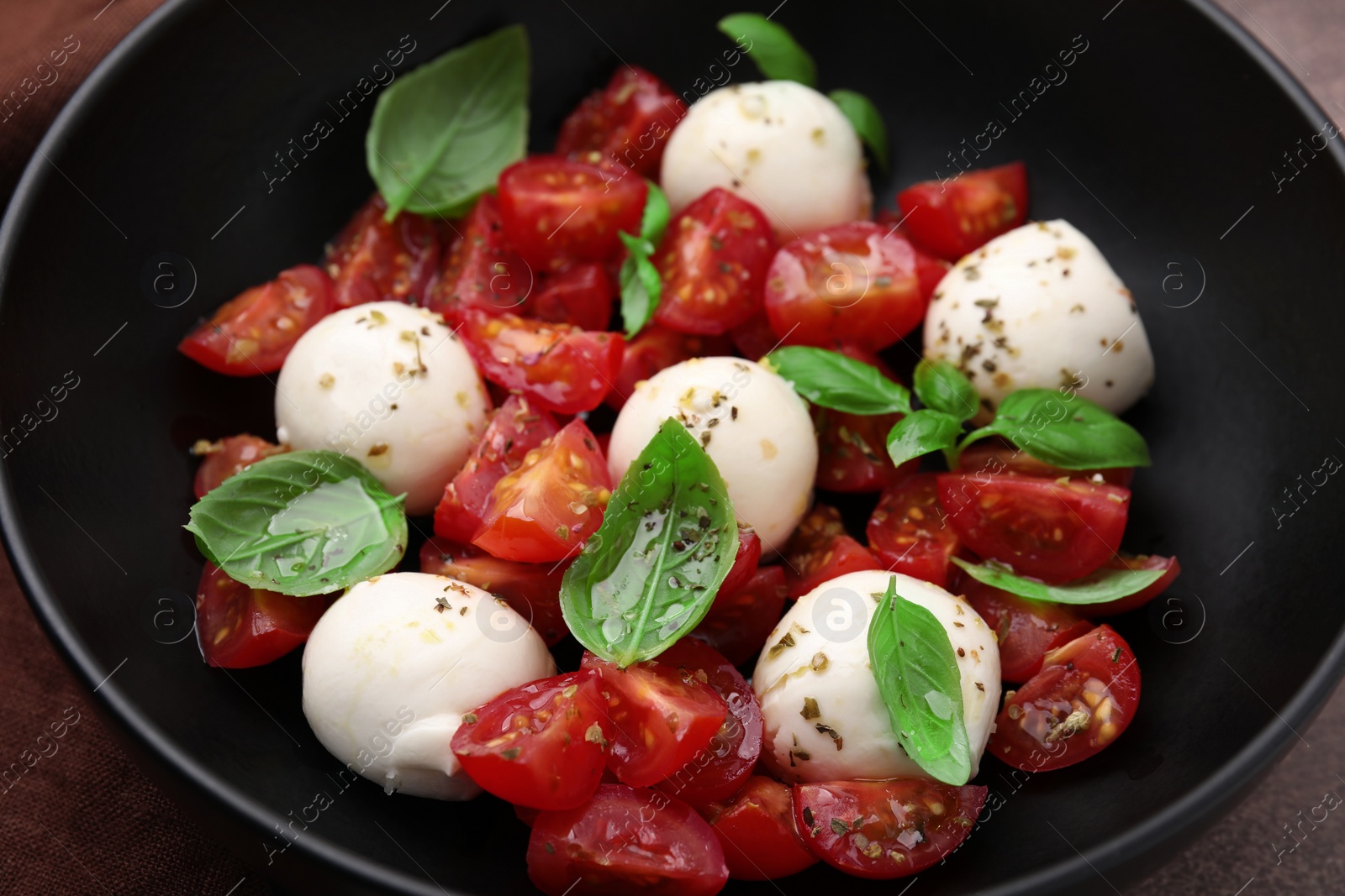 Photo of Tasty salad Caprese with tomatoes, mozzarella balls and basil in bowl, closeup