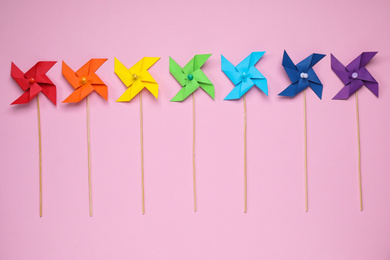 Colorful toy windmills on pink background, flat lay. Rainbow palette