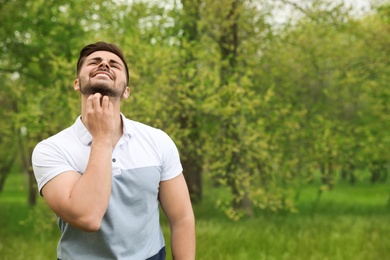 Photo of Young man scratching neck outdoors, space for text. Seasonal allergy