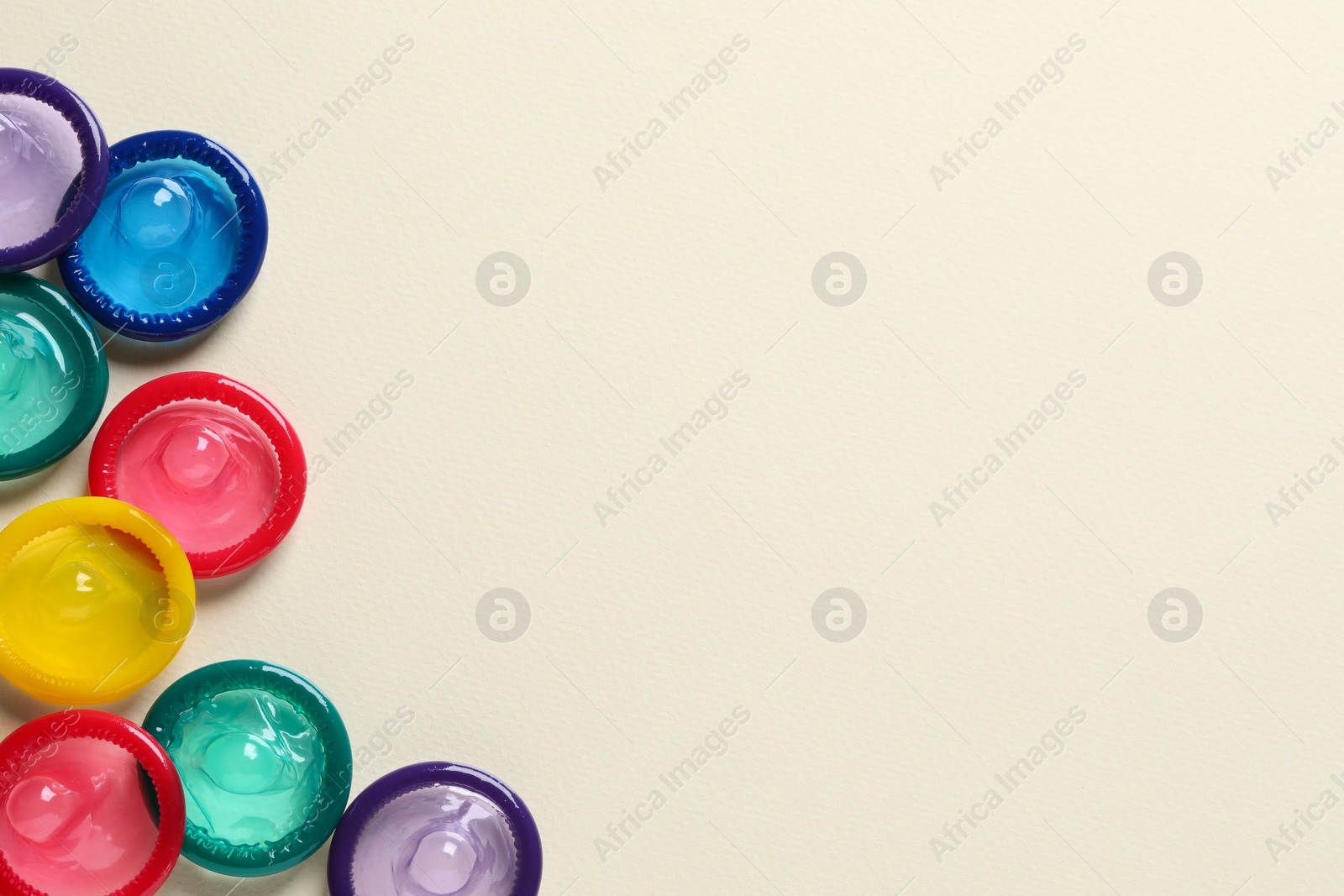 Photo of Colorful condoms on beige background, flat lay. Space for text