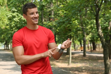 Photo of Young man checking pulse with medical device after training outdoors