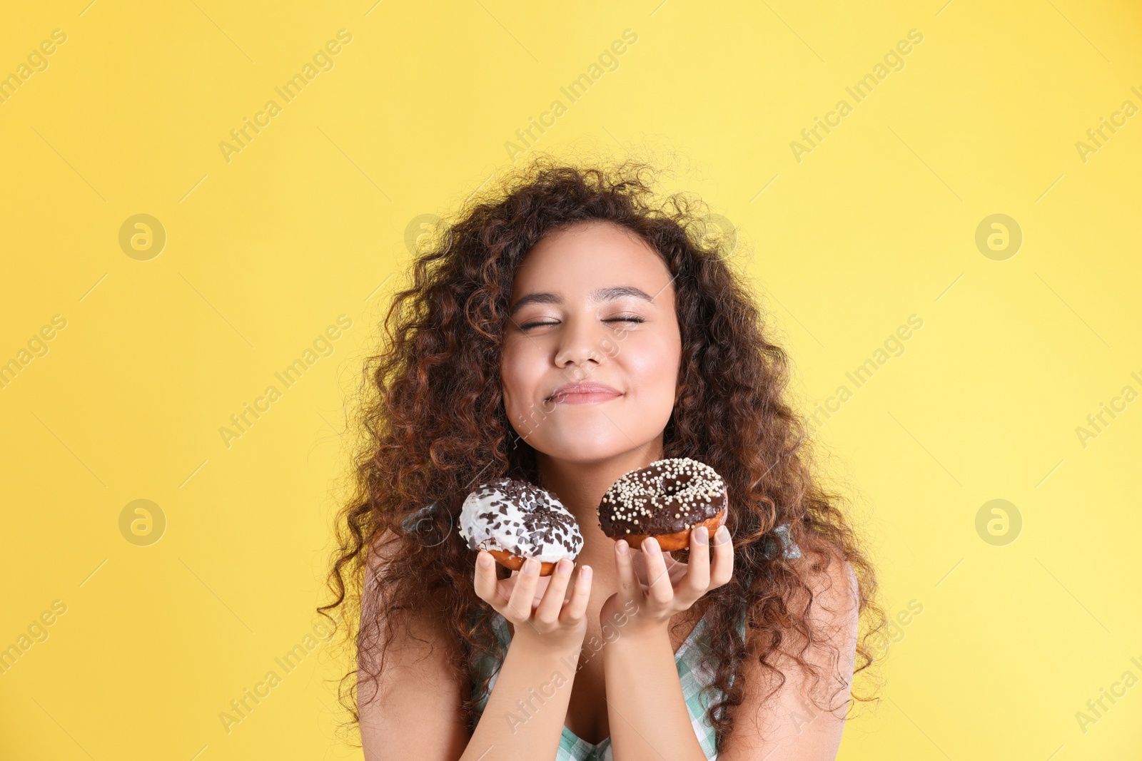 Photo of Beautiful African-American woman with donuts on yellow background