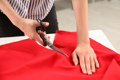 Photo of Woman cutting fabric with sharp scissors at table indoors, closeup