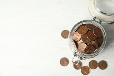 Photo of Glass jar with coins on white wooden table, flat lay. Space for text