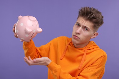 Photo of Upset man with piggy bank on purple background