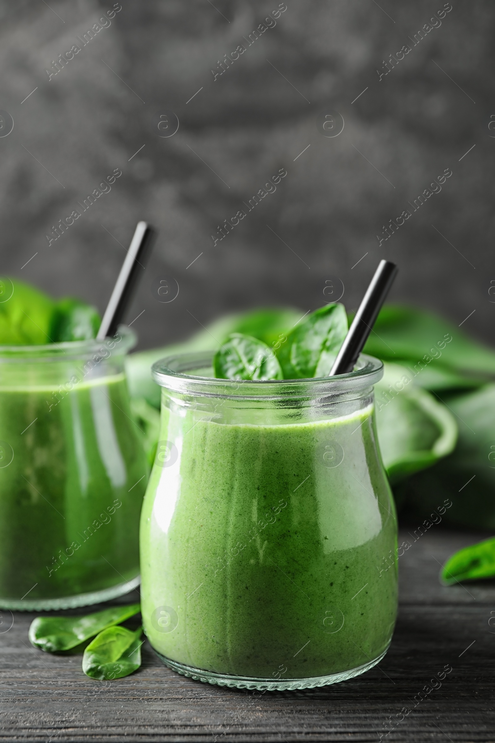 Photo of Jars of healthy green smoothie with fresh spinach on grey wooden table