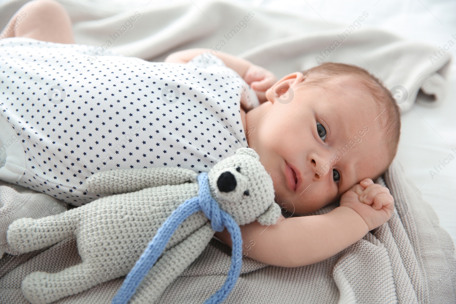 Photo of Adorable newborn baby with toy bear lying on soft blanket