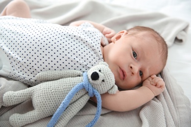 Photo of Adorable newborn baby with toy bear lying on soft blanket