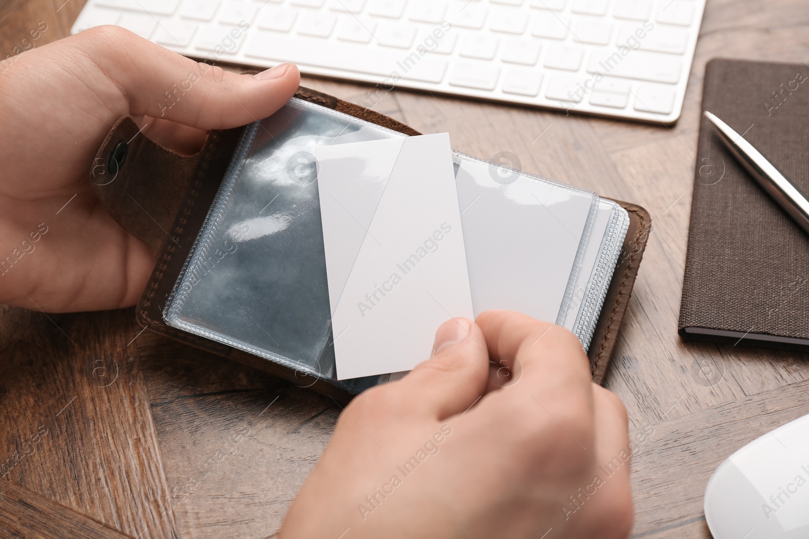 Photo of Man holding leather business card holder with blank cards at wooden table, closeup