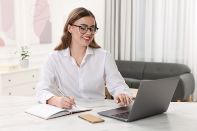 Happy woman with notebook and laptop at white table in room