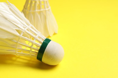 Photo of Feather badminton shuttlecocks on yellow background, closeup. Space for text