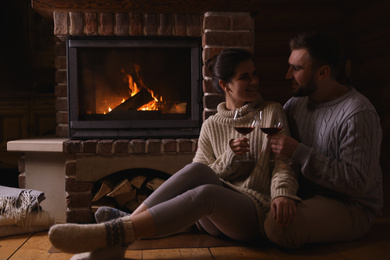 Lovely couple with glasses of wine near fireplace at home. Winter vacation