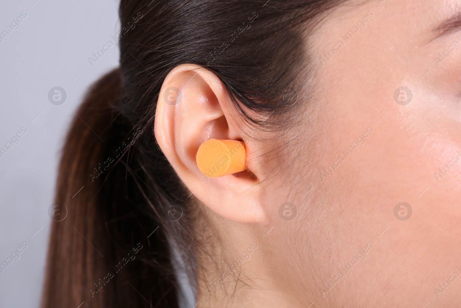 Photo of Young woman wearing foam ear plug on grey background, closeup