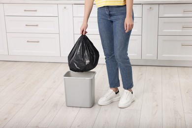 Photo of Woman taking garbage bag out of trash bin in kitchen, closeup